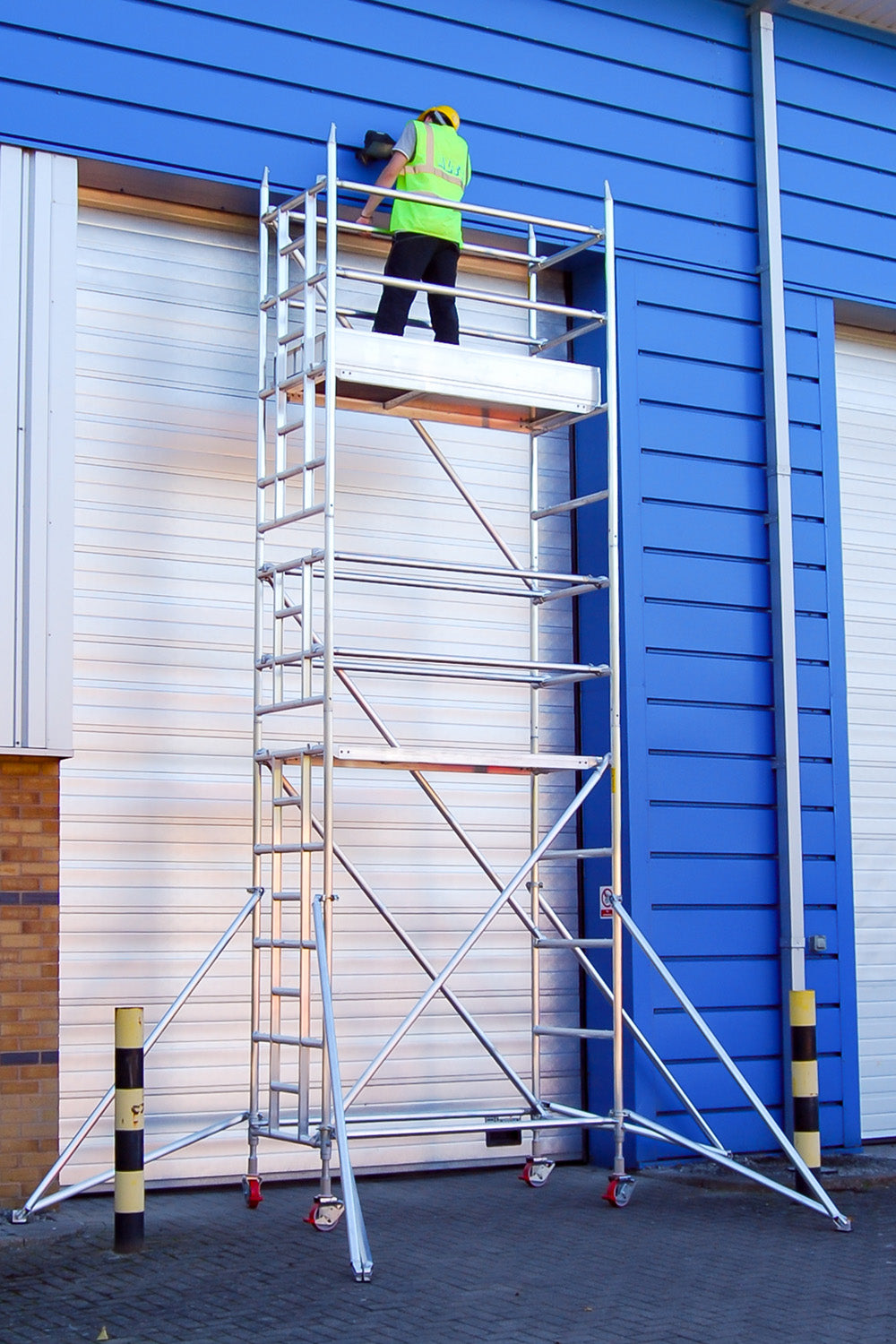 A person working on a single width Alto HD access tower against a silver and blue metal-clad building.