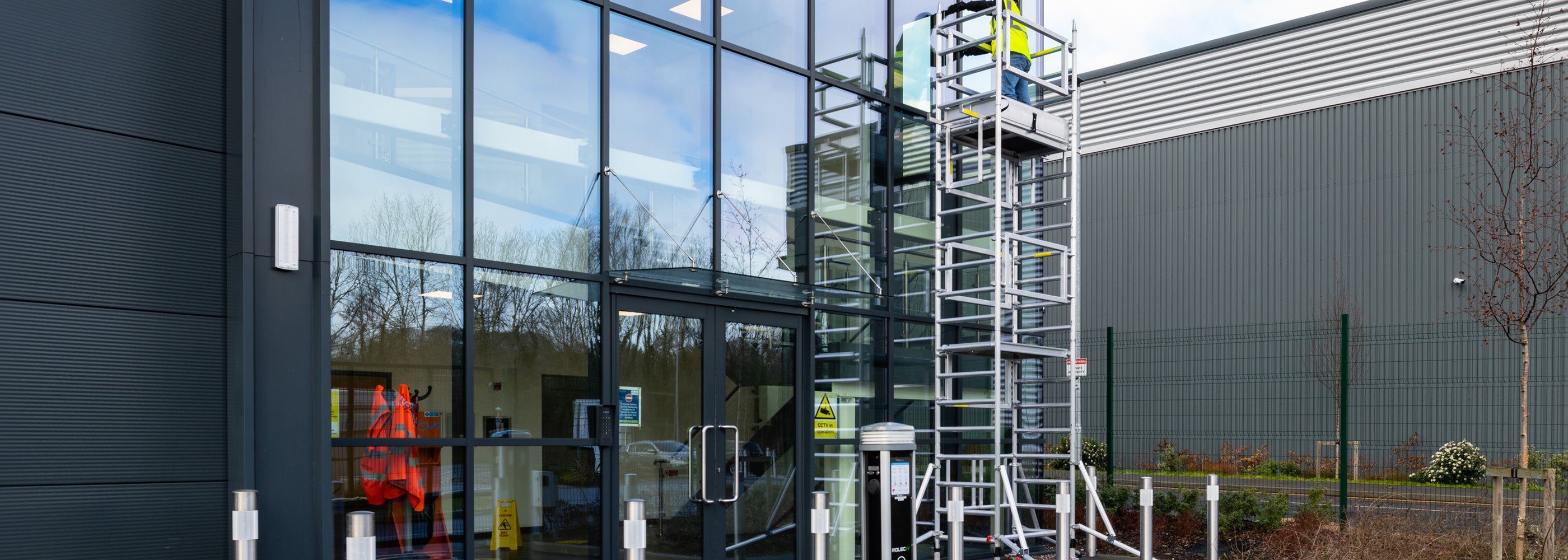 Alto one man tower outside a modern building with glass facade.