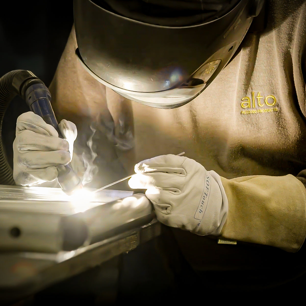 Person welding an Alto Access aluminium frame with a welding torch, wearing protective gear and gloves.